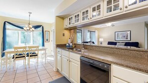 A kitchen with a dishwasher, a dining table with chairs, and a window with blue curtains.