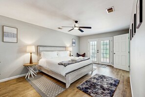 A bedroom with a bed, a ceiling fan, a nightstand with a lamp, and a door leading to another room. - Updated Pet-Friendly Home Near Park Circle, Charleston & Beaches (Charleston)