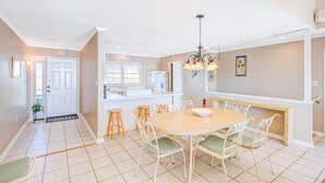 Uma cozinha ampla com uma ilha central, armários brancos e uma área de jantar com mesa e cadeiras redondas.