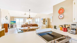 Uma cozinha moderna com uma ilha central, um espaço de jantar com mesa redonda e uma sala de estar com sofá e televisão.