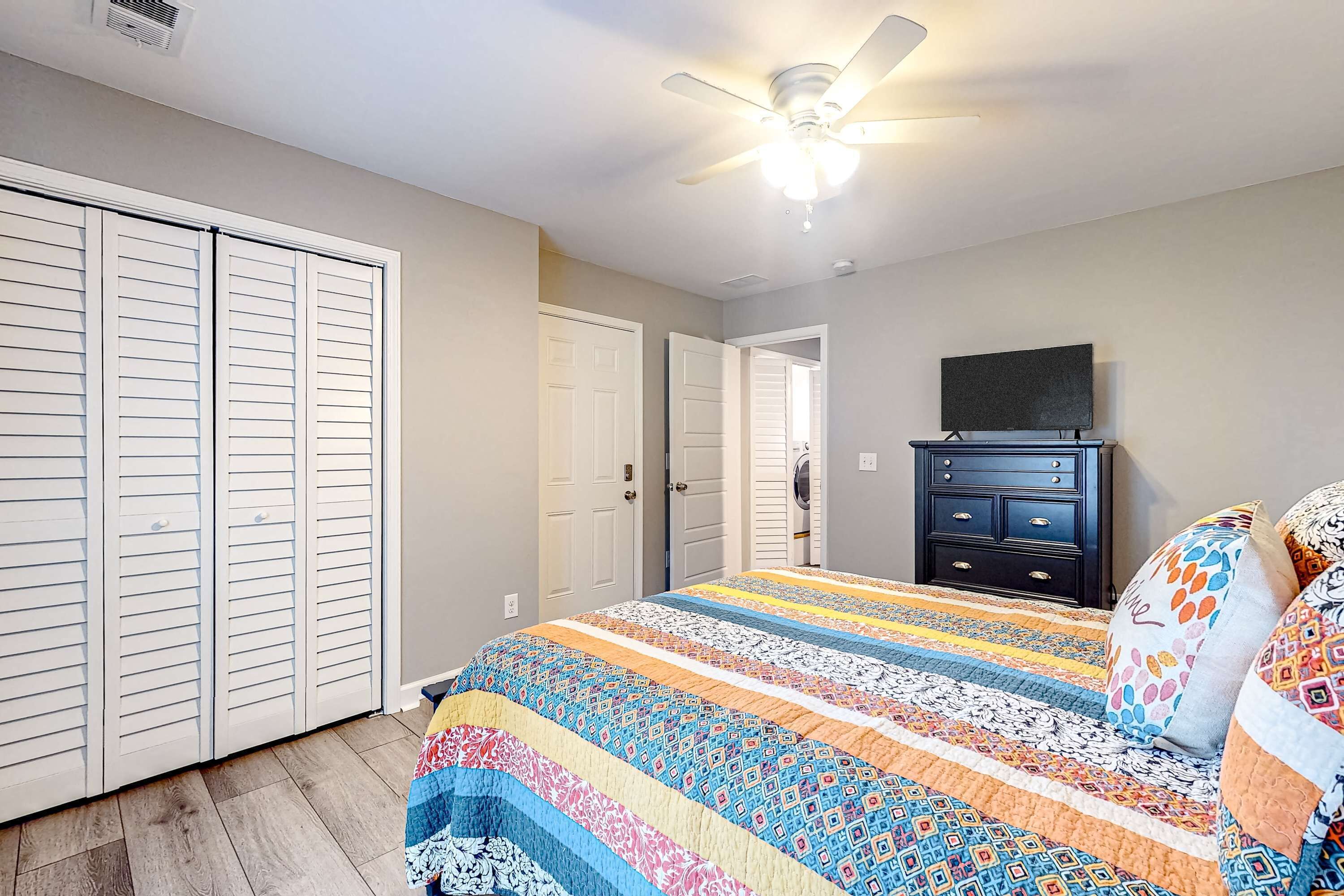 A bedroom with a large bed, a ceiling fan, a dresser, and a TV.
