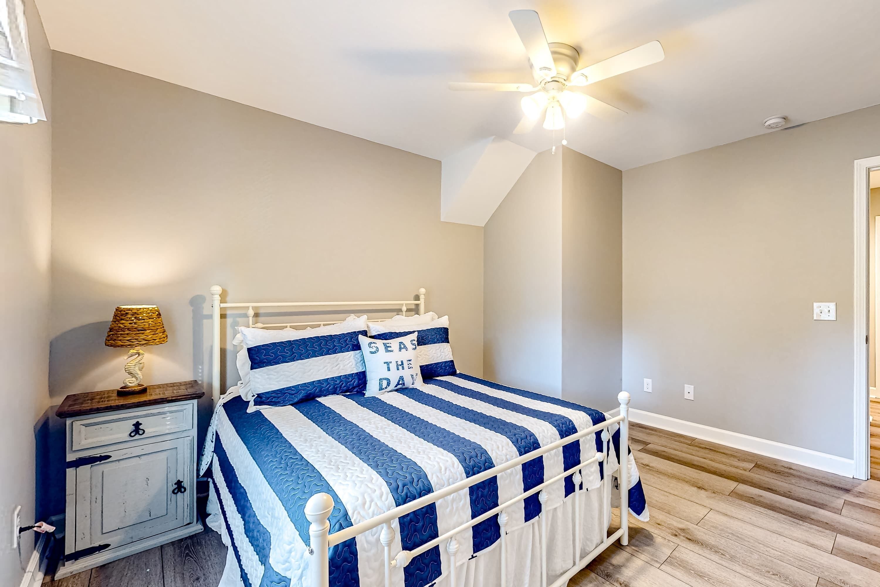 Un dormitorio con cama, mesita de noche, lámpara, ventilador de techo y suelo de madera.