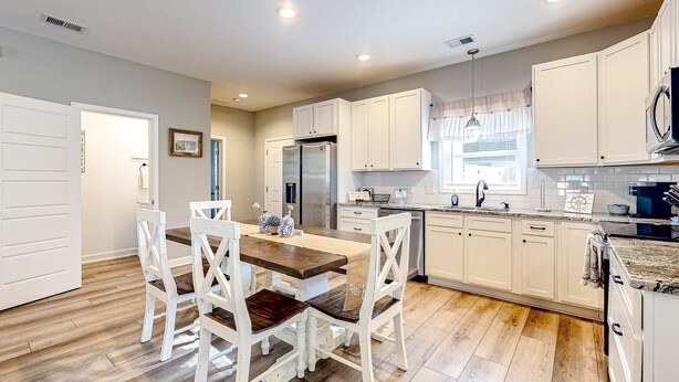 Una cocina moderna con armarios blancos, una mesa de comedor de madera y un refrigerador de acero inoxidable.