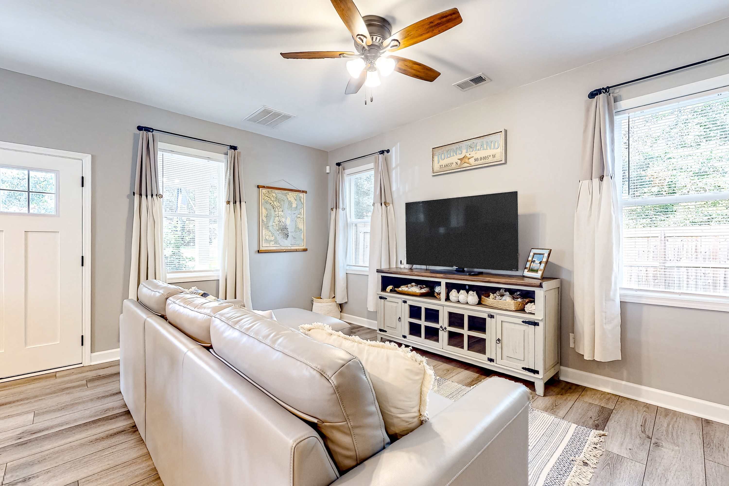 Un salon avec un canapé en cuir, un téléviseur posé sur un meuble et un ventilateur de plafond.