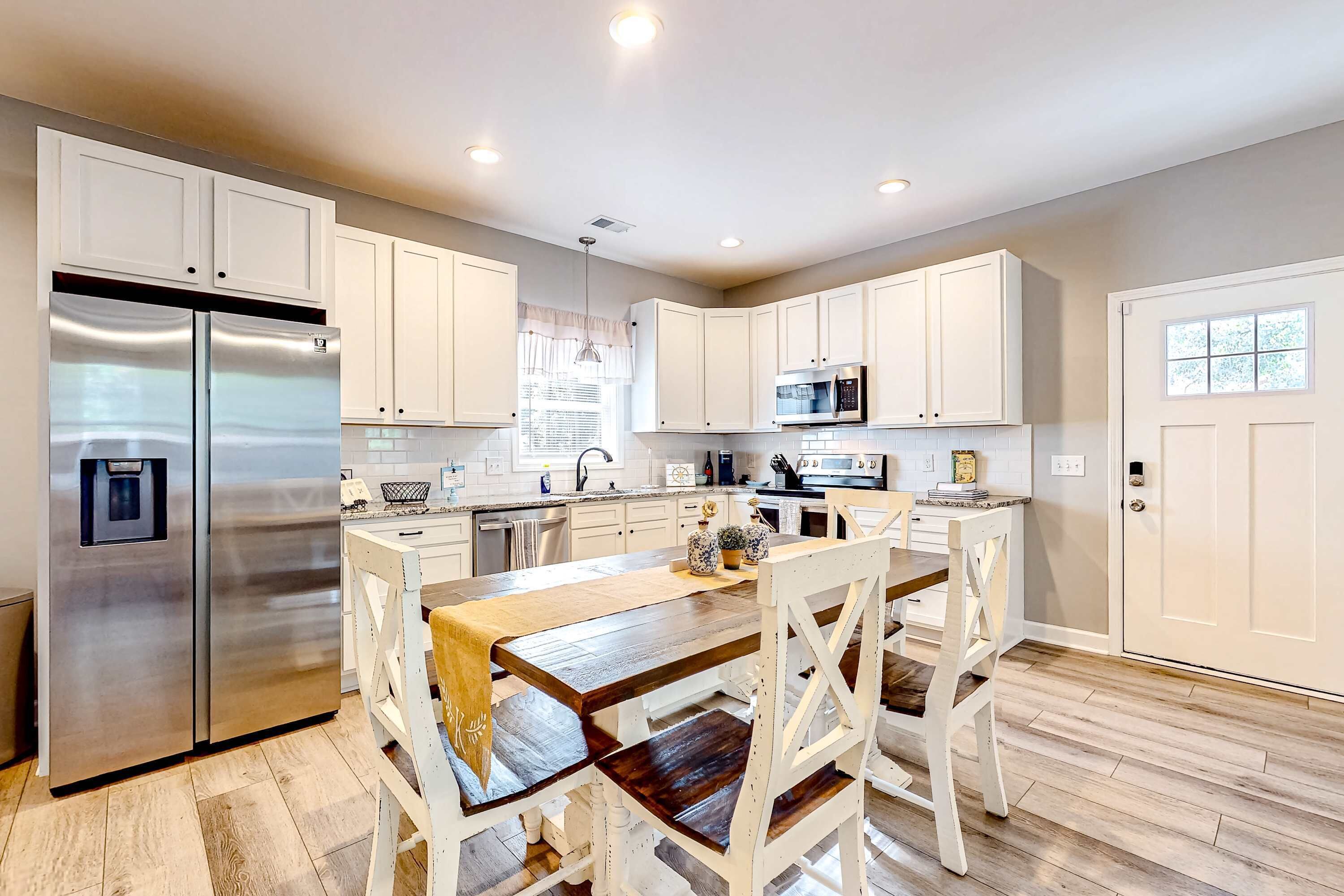 Una cocina moderna con armarios blancos, electrodomésticos de acero inoxidable y una mesa de comedor de madera.