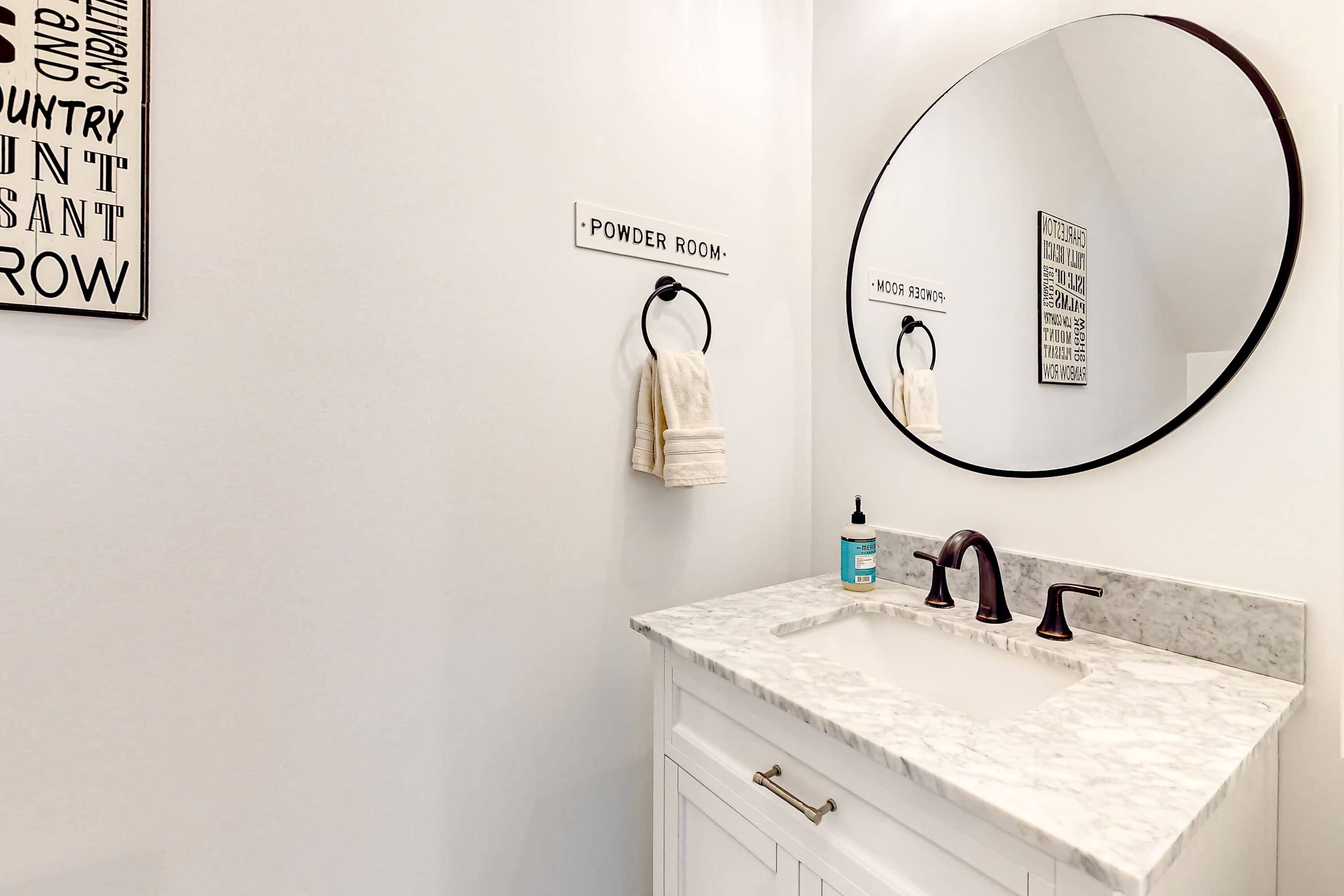 Une salle de bain avec un meuble-lavabo blanc, un miroir rond et un panneau indiquant les toilettes.