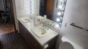 Une salle de bain avec deux lavabos, un miroir avec éclairage intégré, des toilettes et un espace douche.
