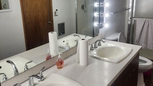 Une salle de bain avec deux lavabos, un miroir avec éclairage intégré, une douche et des toilettes.