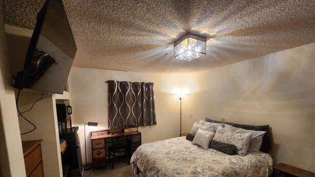 Une chambre à coucher comprenant un lit, un bureau, une chaise et un luminaire fixé au plafond.