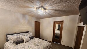 Une chambre avec un grand lit, une porte en bois et un luminaire au plafond.
