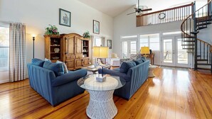 A spacious living room with a high ceiling, a wooden staircase, and a large window. - Spacious oceanfront home w/ stunning views, large deck - private access to beach (Folly Beach)