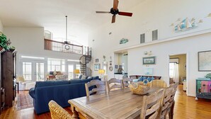 A spacious living area with a dining table, sofas, and a staircase leading to an upper level. - Spacious oceanfront home w/ stunning views, large deck - private access to beach (Folly Beach)