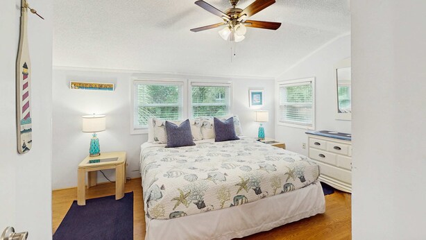 A bedroom with a bed, nightstands, a dresser, a ceiling fan, and a window with blinds.