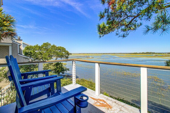 A balcony with a view of a calm body of water, a wooden deck, and a blue Adirondack chair. - Centrally located to local attractions, close to beach access & marsh views (Isle of Palms)