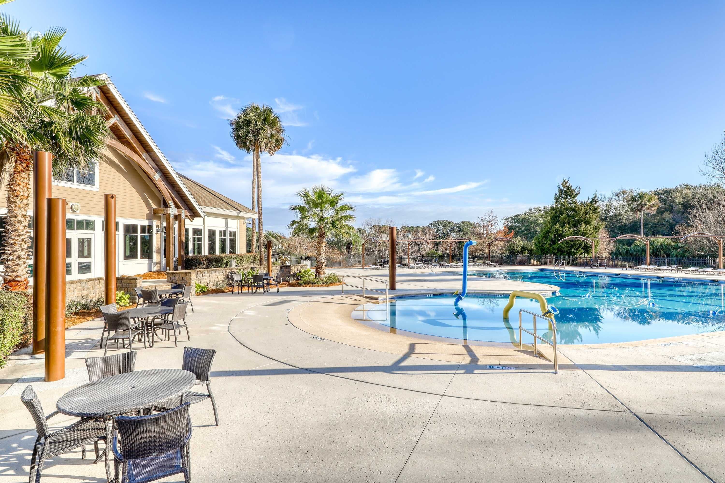A pool area with a curved patio, outdoor seating, and a building with large windows.