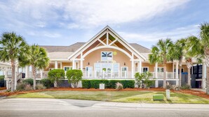 A two-story building with a beige facade, a central entrance with a white railing, and palm trees surrounding the property. - Dog friendly villa (Seabrook Island)