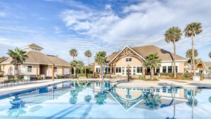 A swimming pool with clear blue water, surrounded by palm trees and a building with a gabled roof. - Dog friendly villa (Seabrook Island)