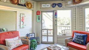 Ein vom Strand inspiriertes Zimmer mit Rattanmöbeln, einem Glastisch und dekorativen Wandbildern.