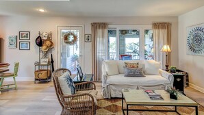 Ein Wohnzimmer mit einer Couch, einem Couchtisch, Korbstühlen und einem Essbereich mit Tisch und Stühlen.