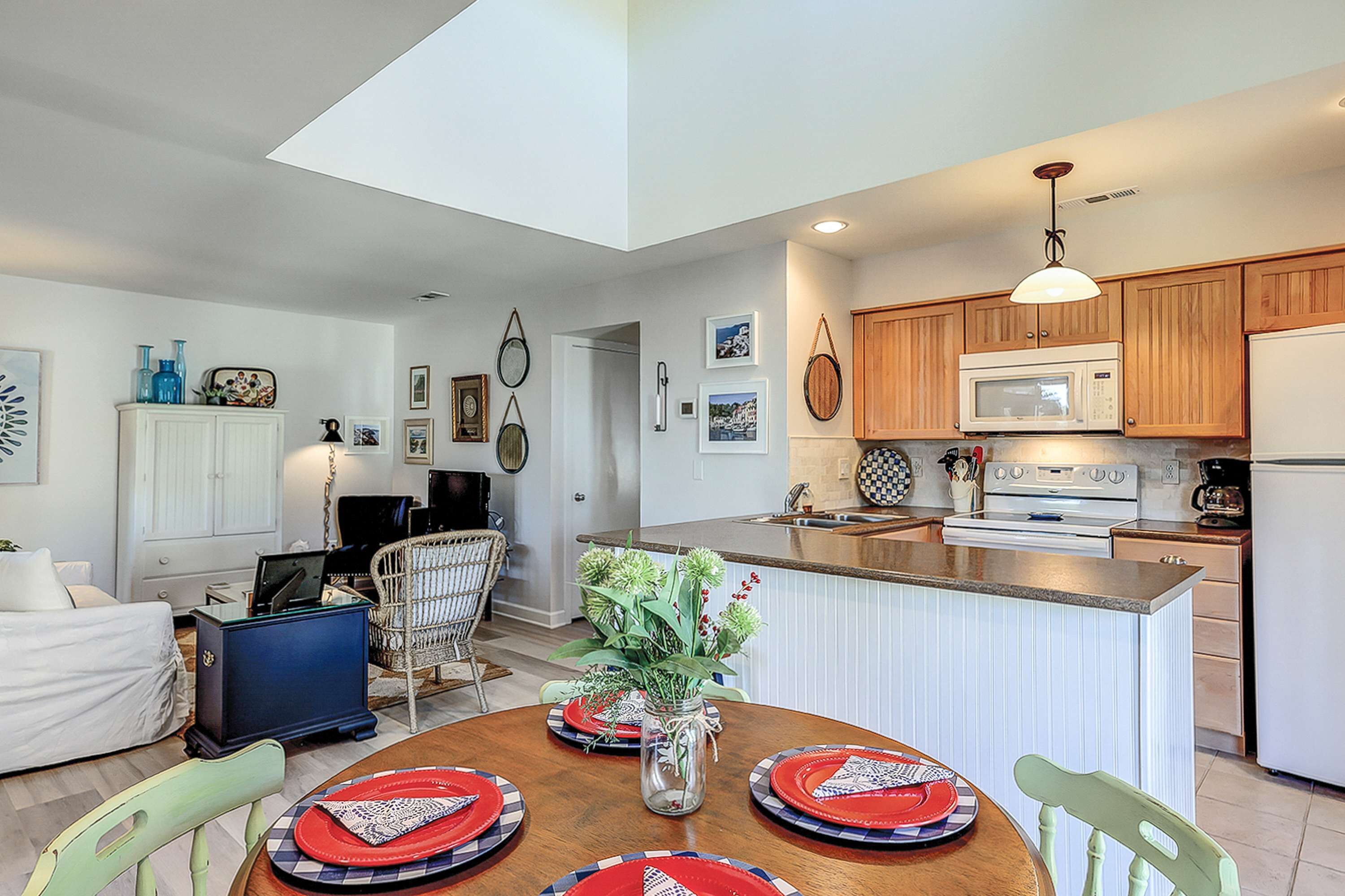 A modern kitchen with wooden cabinets, a microwave, and a refrigerator. There is a dining area with a table set for four, featuring red and blue plates.