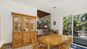A dining area with a wooden table and chairs, a cabinet with glass doors, and a view through a large window.