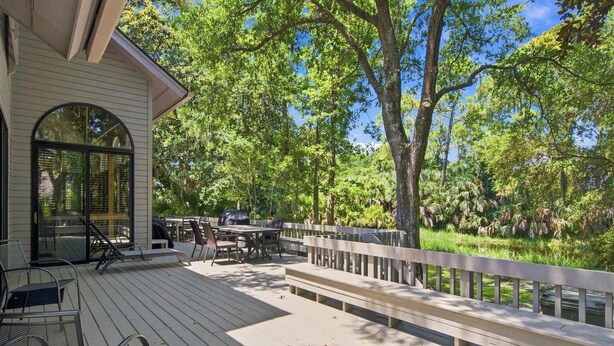 A wooden deck with outdoor furniture, a covered grill, and a view of a forested area.