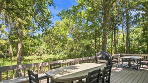 An outdoor deck with a table and chairs, surrounded by a wooden railing, overlooking a forested area.