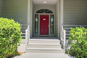 A front porch with a red door, a small set of steps, and two bushes on either side.