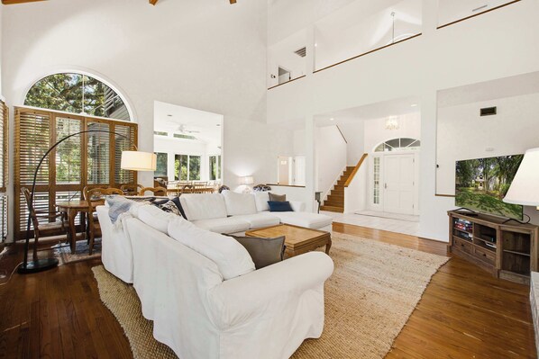 A spacious living room with a white sofa, wooden dining table, and a staircase leading to an upper level.