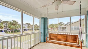 A porch with a wooden swing, white railing, and large windows overlooking a residential area.