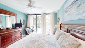 Een slaapkamer met een bed, dressoir, televisie en plafondventilator.