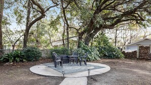 A patio with a table and chairs, surrounded by trees and a house in the background. - Darling, renovated home w/ beautiful backyard, W/D & WiFi - near beaches (Mt. Pleasant)