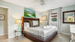 A bedroom with a large bed, a ceiling fan, a window with curtains, and a bedside table with lamps. - Darling, renovated home w/ beautiful backyard, W/D & WiFi - near beaches (Mt. Pleasant)