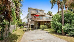 A two-story house with a balcony, a covered patio, and a driveway leading to the entrance. - Relaxing oceanside home w/ multiple decks, outdoor shower- steps to beach access (Folly Beach)