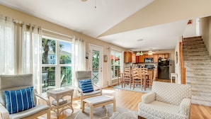 A spacious living room with a sofa, chairs, and a dining area. A staircase leads to a kitchen and dining area. - Relaxing oceanside home w/ multiple decks, outdoor shower- steps to beach access (Folly Beach)