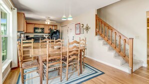 A spacious kitchen with wooden cabinets, a dining table with chairs, and a staircase with a wooden railing. - Relaxing oceanside home w/ multiple decks, outdoor shower- steps to beach access (Folly Beach)