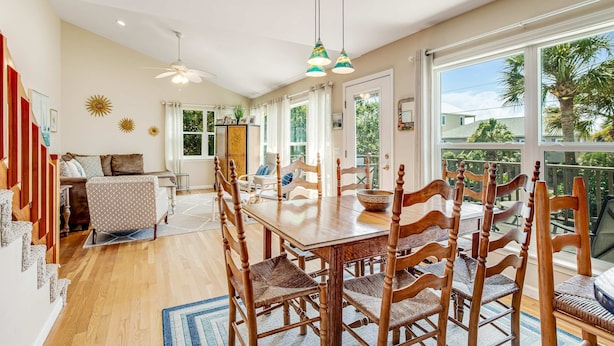 A spacious dining area with a wooden table and chairs, large windows with a view of palm trees, and a ceiling fan. - Relaxing oceanside home w/ multiple decks, outdoor shower- steps to beach access (Folly Beach)