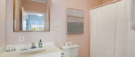 A bathroom with a white sink, mirror, toilet, and shower curtain.