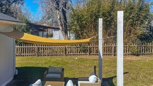 Un patio trasero con zona de estar, mobiliario de mimbre y una vela de sombra amarilla.