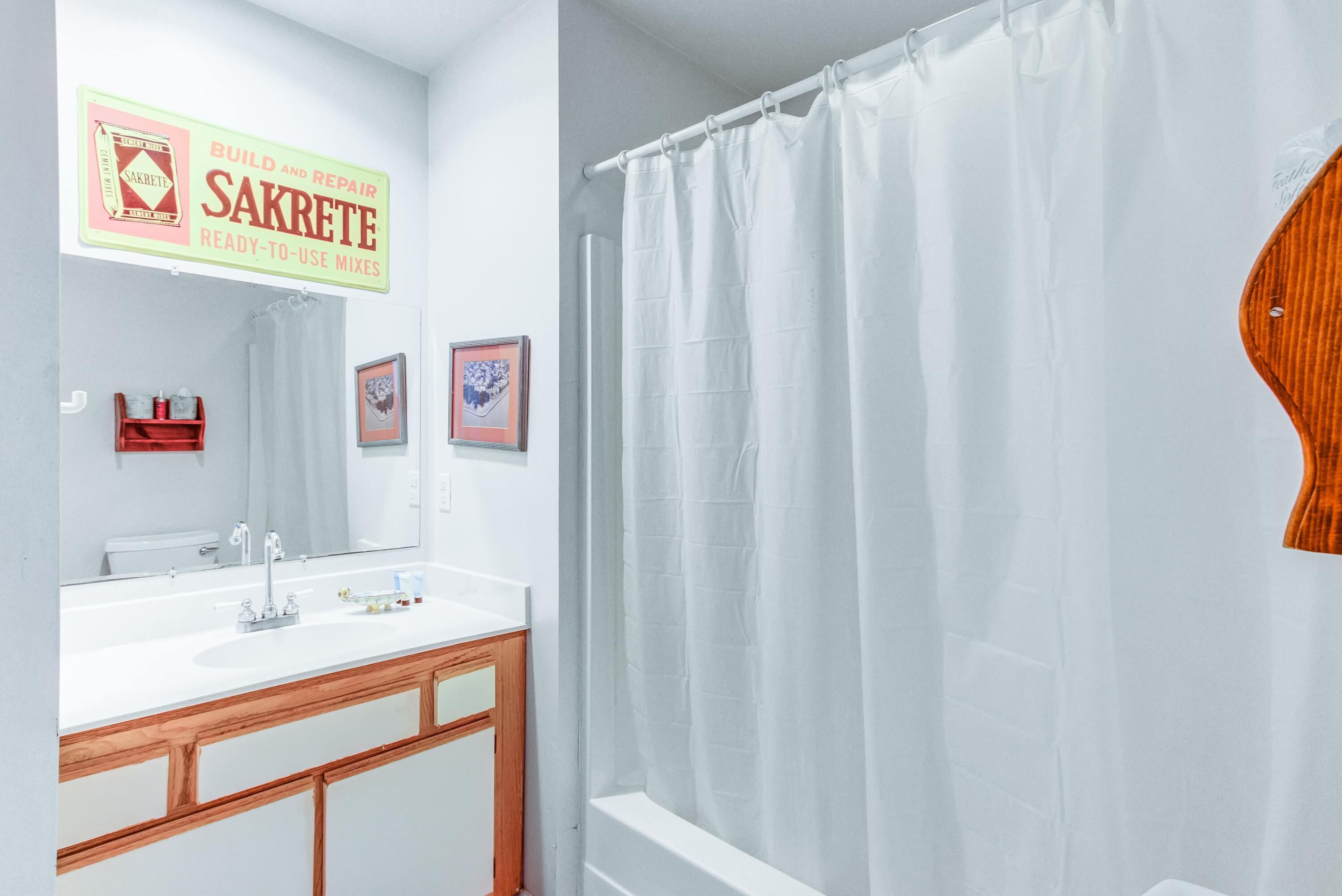 Baño con lavamanos blanco, tocador de madera y cortina de ducha.