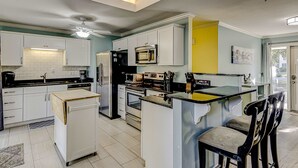 Une cuisine moderne avec des meubles blancs, un îlot central doté de tabourets, un four à micro-ondes et une cuisinière.