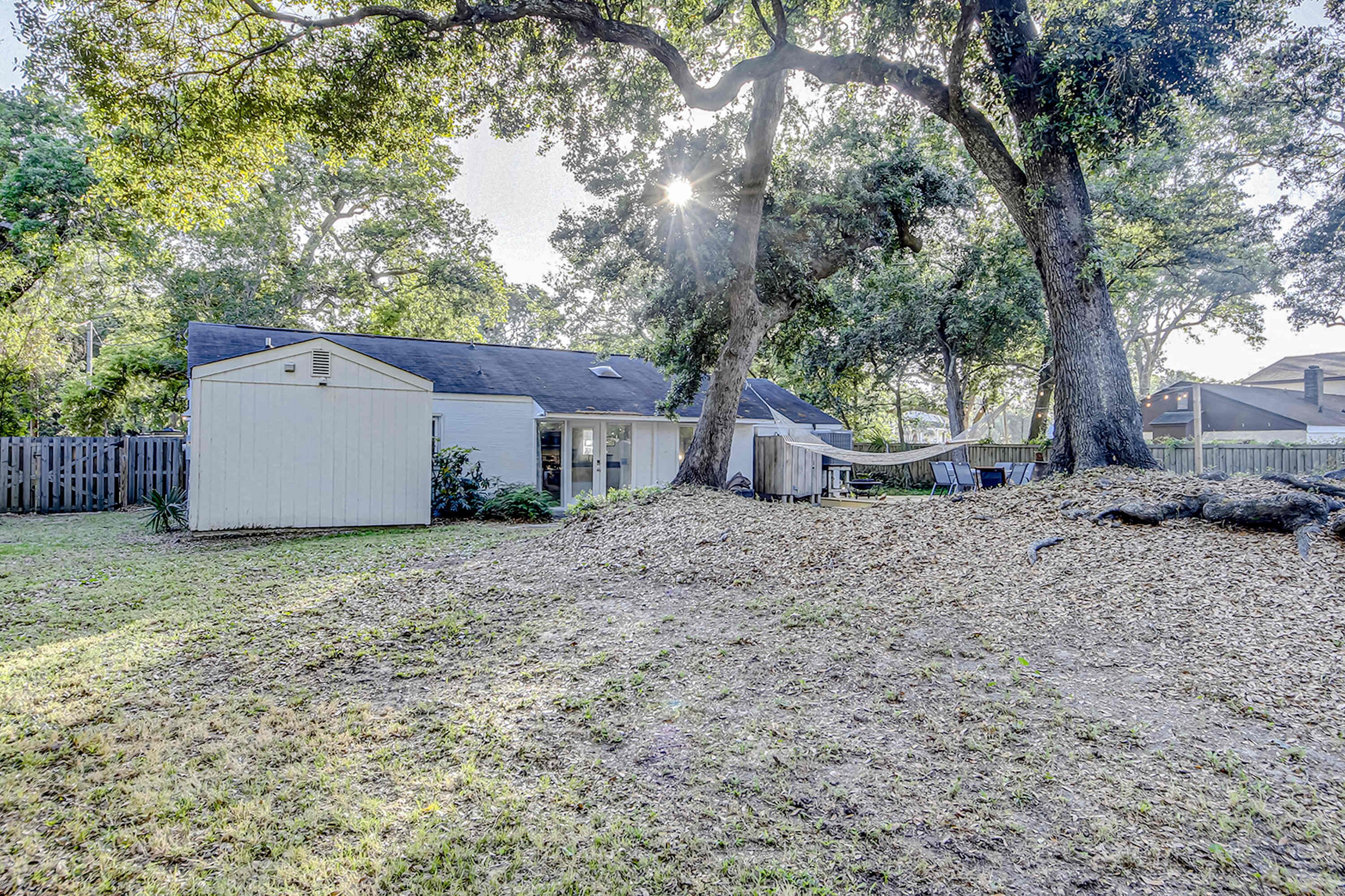 A residential area with a white shed, a covered outdoor seating area, and a large tree providing shade.