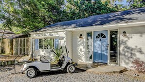 Une maison blanche avec une allée en gravier et un véhicule de golf garé devant.