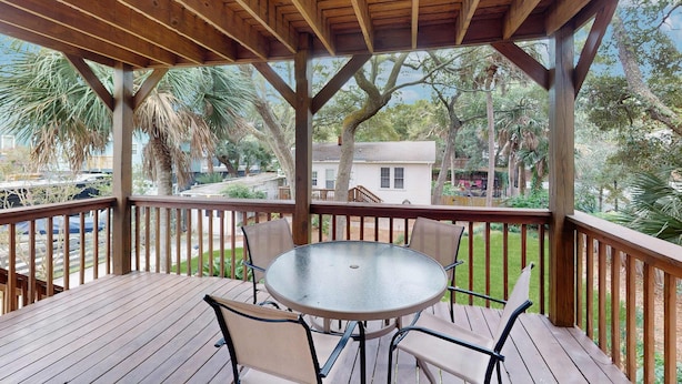 A wooden deck with a glass table and chairs, overlooking a residential area with palm trees and a house. - Amazing Beach Home (Folly Beach)