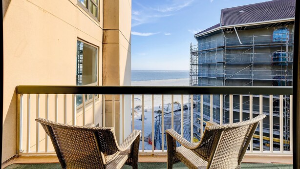 Un balcone con sedie in vimini, vista sull'oceano e un edificio in costruzione con ponteggi.