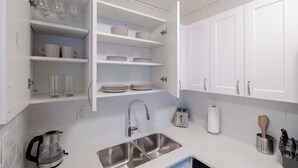 Una cocina moderna con armarios blancos, un lavamanos de acero inoxidable, una tetera y diversos utensilios de cocina.