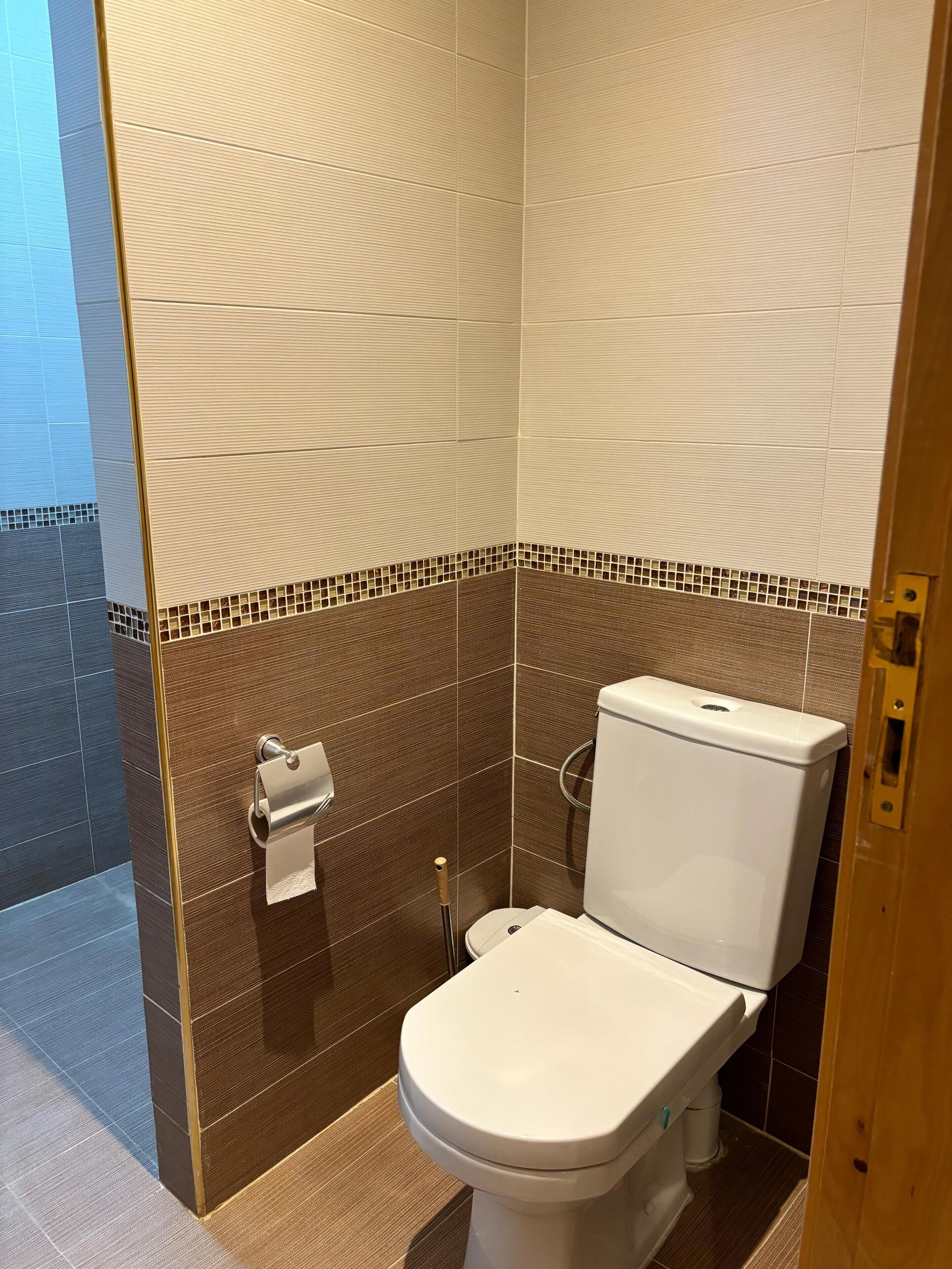 Een badkamer met een toilet, een papieren handdoekdispenser en een douchegedeelte.