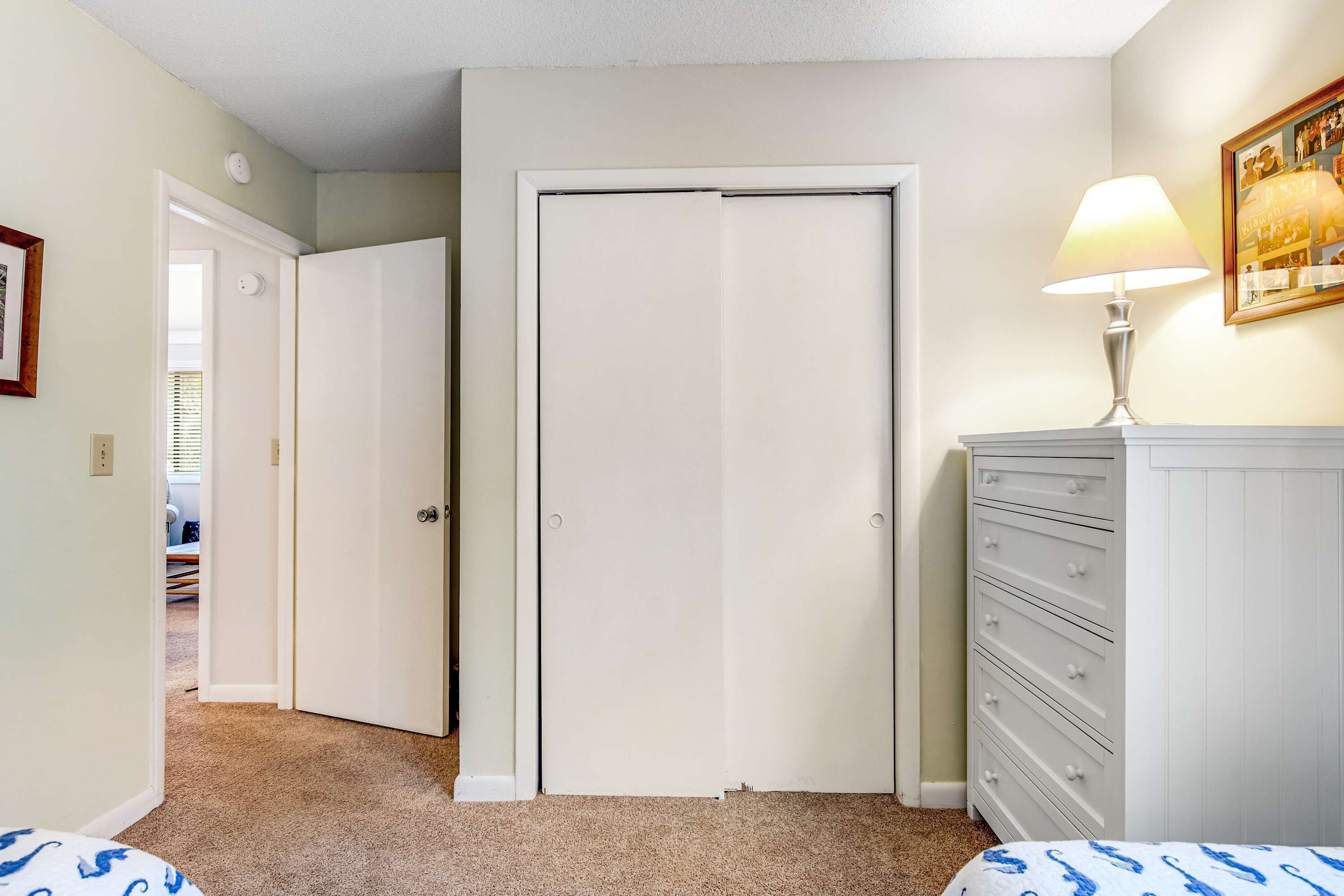 A bedroom with a closed door, a dresser, a lamp, and a framed picture on the wall.