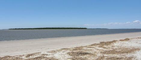 Ein Strand mit sandigem Ufer und einer kleinen Insel in der Ferne.
