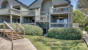 A multi-story building with balconies, a wooden staircase, and a well-maintained lawn. - Condo with sunset views, with ocean/inlet views - walk to the Beach Club (Seabrook Island)